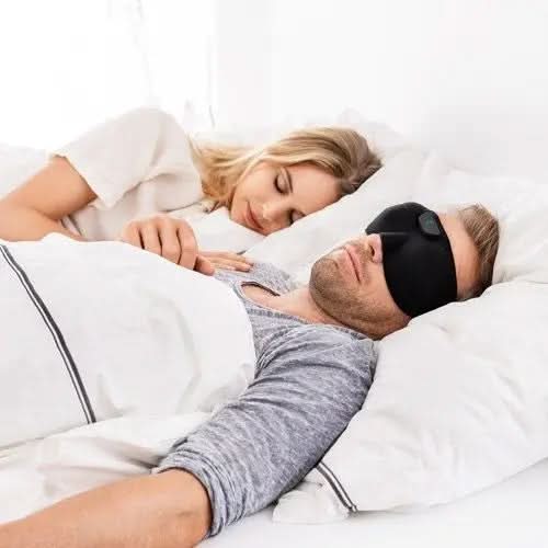 Homme dormant avec un masque massage haute technologie noir dans un lit avec une femme à ses côtés